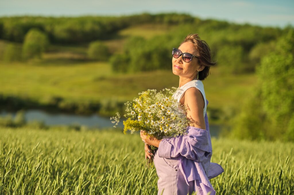 The Asian woman, amidst wheat, holds flowers high; her tranquility a silent narrative on menopause
